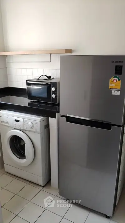 Modern kitchen with washing machine, microwave, and sleek fridge in compact layout.