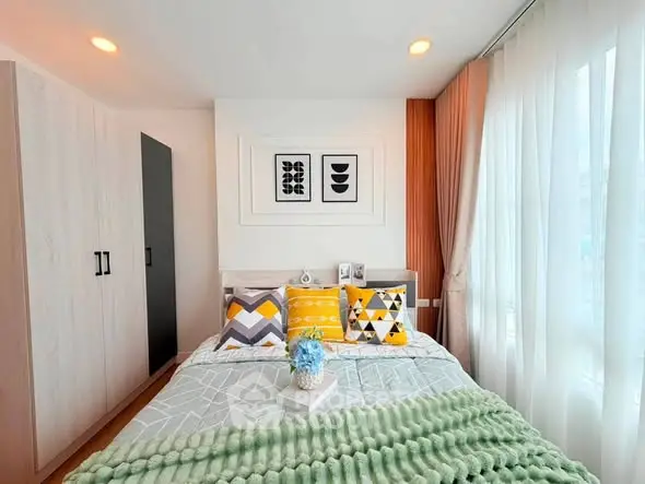 Chic bedroom with modern decor, vibrant pillows, and ample natural light from large windows.