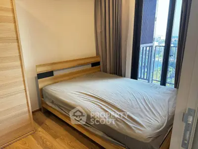 Cozy bedroom with wooden flooring and large window offering city view.