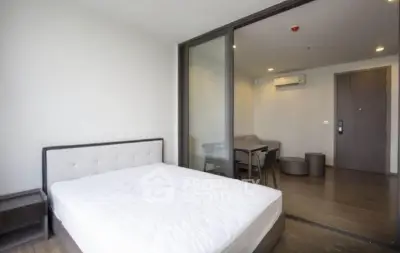 Modern bedroom with sliding glass doors leading to a cozy living area, featuring minimalist design and ample natural light.
