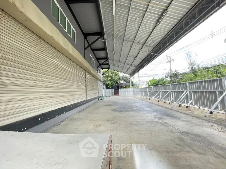 Spacious industrial warehouse with large covered loading area and secure fencing.