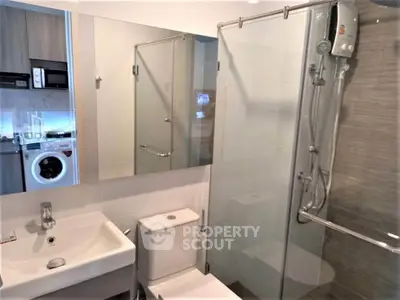 Modern bathroom with glass shower and washing machine in compact layout.