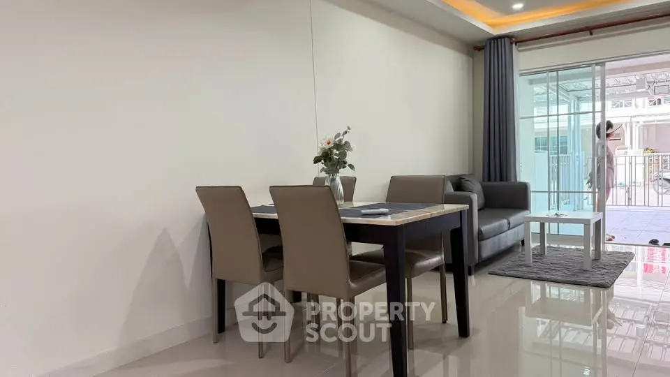 Modern living room with dining area and large windows leading to a balcony, featuring sleek furniture and elegant decor.