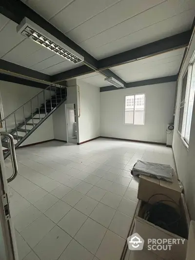 Spacious industrial-style room with staircase and large windows, ideal for office or studio space.