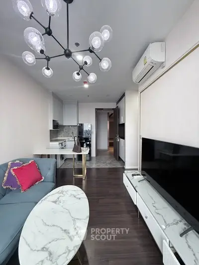 Modern living room with stylish chandelier, sleek furniture, and open kitchen layout in a contemporary apartment.
