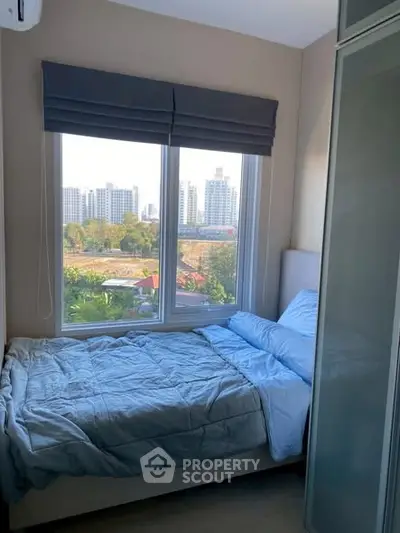 Cozy bedroom with large window offering stunning cityscape views, perfect for urban living.
