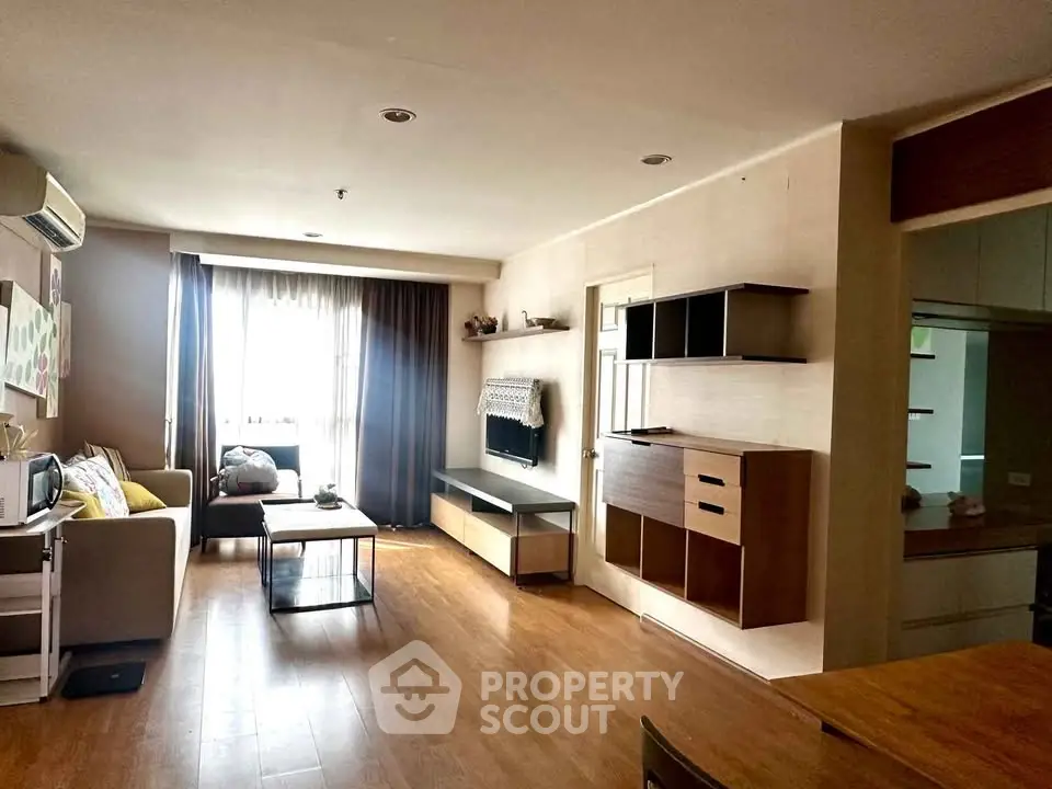 Spacious living room with modern decor and natural light, featuring wooden flooring and stylish furniture.