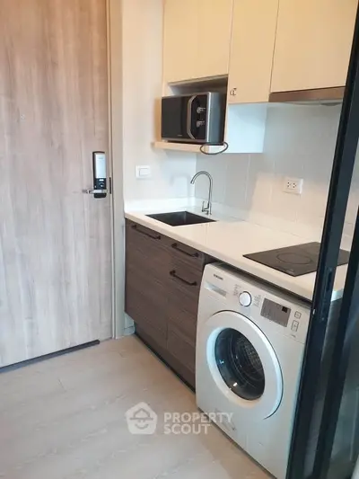 Modern compact kitchen with washing machine and microwave in stylish apartment.