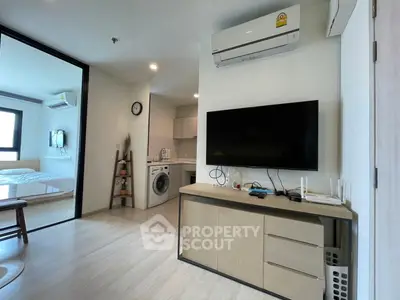 Modern apartment interior with open living area, TV, and kitchen appliances.