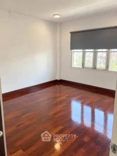 Spacious empty room with polished wooden floors and large window, perfect for customization.