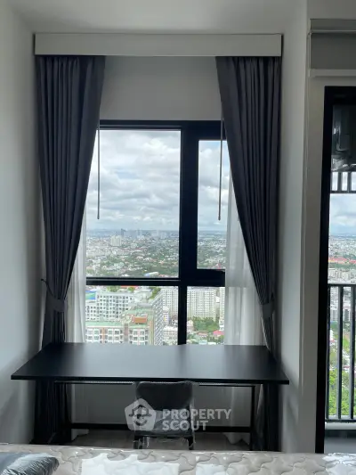 Modern high-rise apartment with stunning city view from bedroom window, featuring sleek desk and chair setup.
