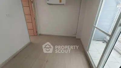 Spacious empty room with wooden flooring and large window for natural light.