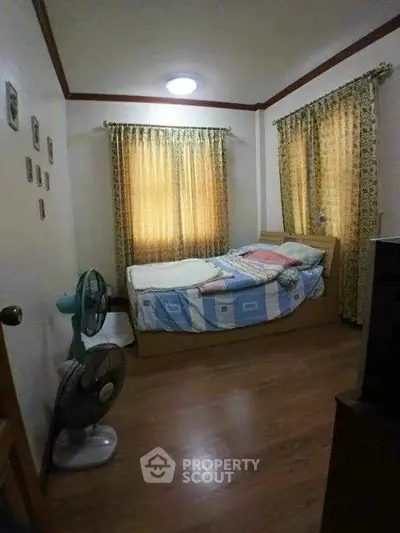 Cozy bedroom with wooden flooring and natural light through curtains.