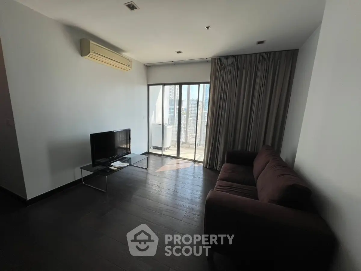 Modern living room with dark wood flooring, sofa, TV, and balcony access.
