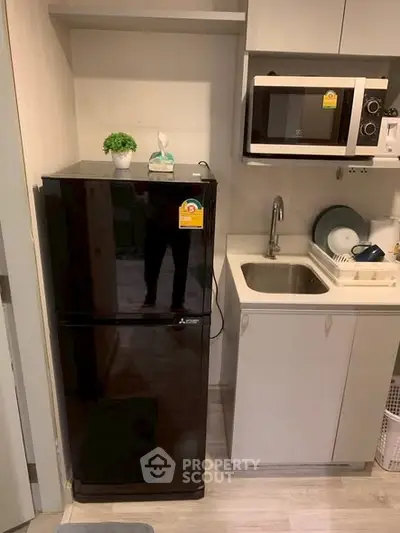 Compact kitchen with black fridge, microwave, and sink in modern apartment.