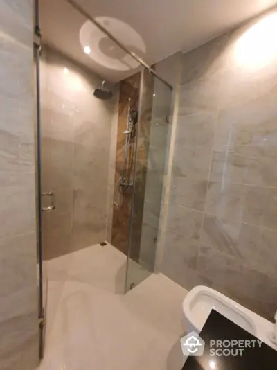 Modern bathroom with elegant marble tiling, glass shower enclosure, and sleek fixtures, perfect for a luxurious home spa experience.