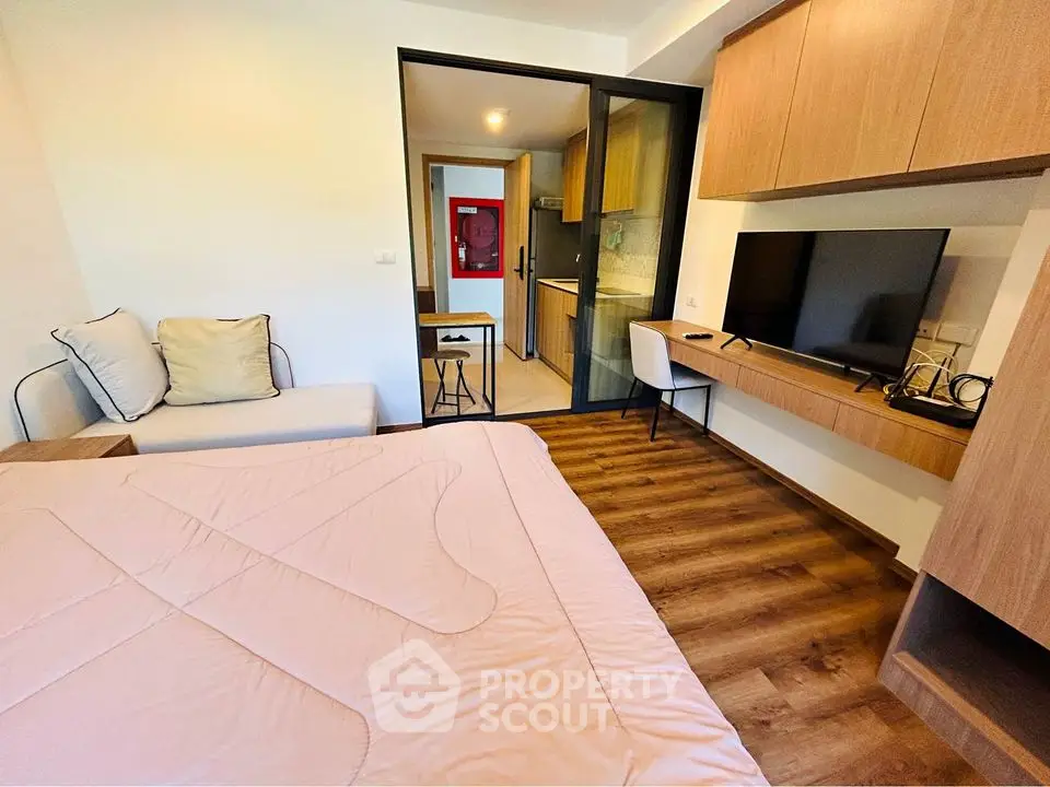 Modern bedroom with wooden flooring and built-in TV unit, adjacent to a compact kitchen.