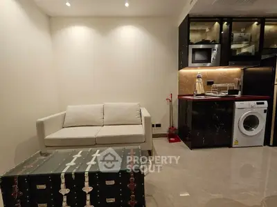 Modern living room with chic sofa and compact kitchen featuring washing machine and microwave.