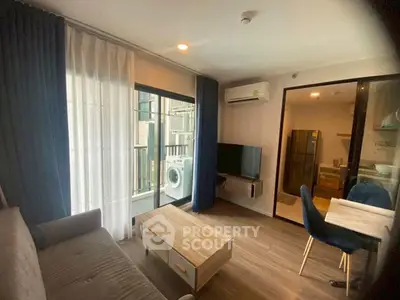 Modern living room with balcony and kitchen view, featuring sleek furniture and natural light.