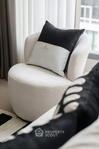 Cozy modern living room with plush white chair and stylish pillow by a window.