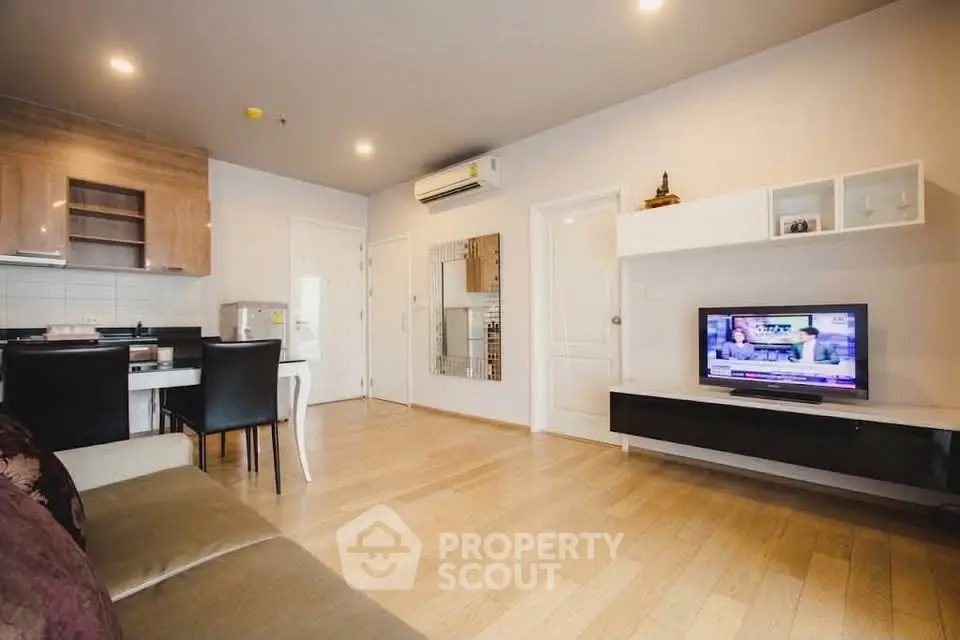 Modern living room with wooden flooring, stylish furniture, and wall-mounted TV in a cozy apartment.