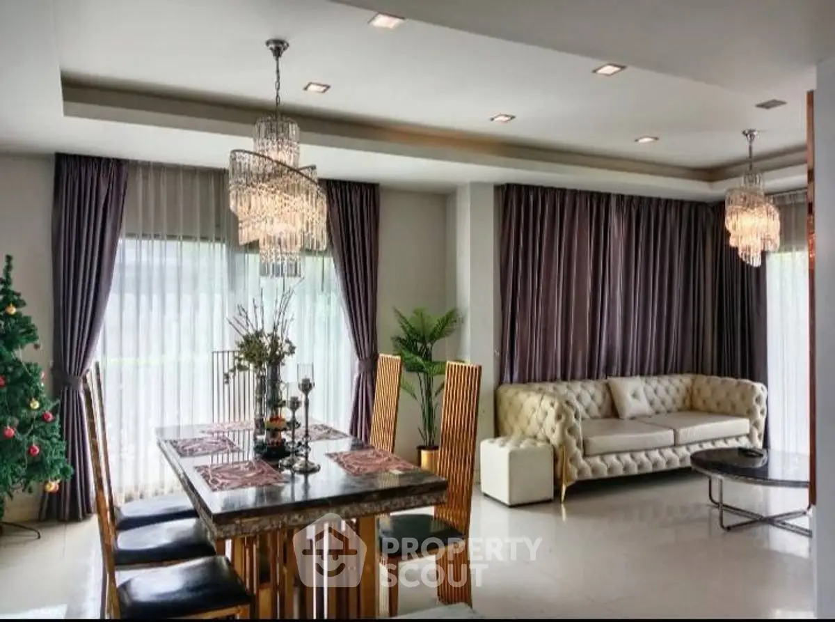 Luxurious living room with elegant dining area and plush sofa, featuring modern chandeliers and large windows.
