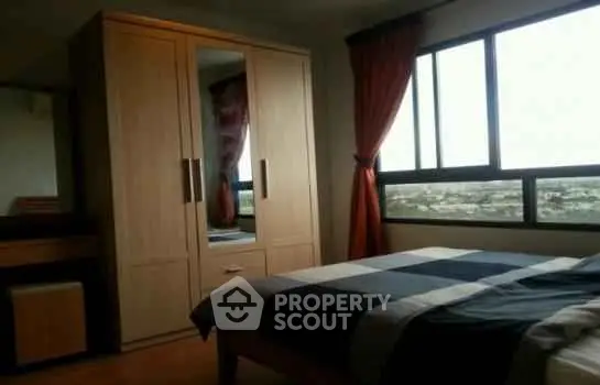 Cozy bedroom with large window and wooden wardrobe, offering a serene view.