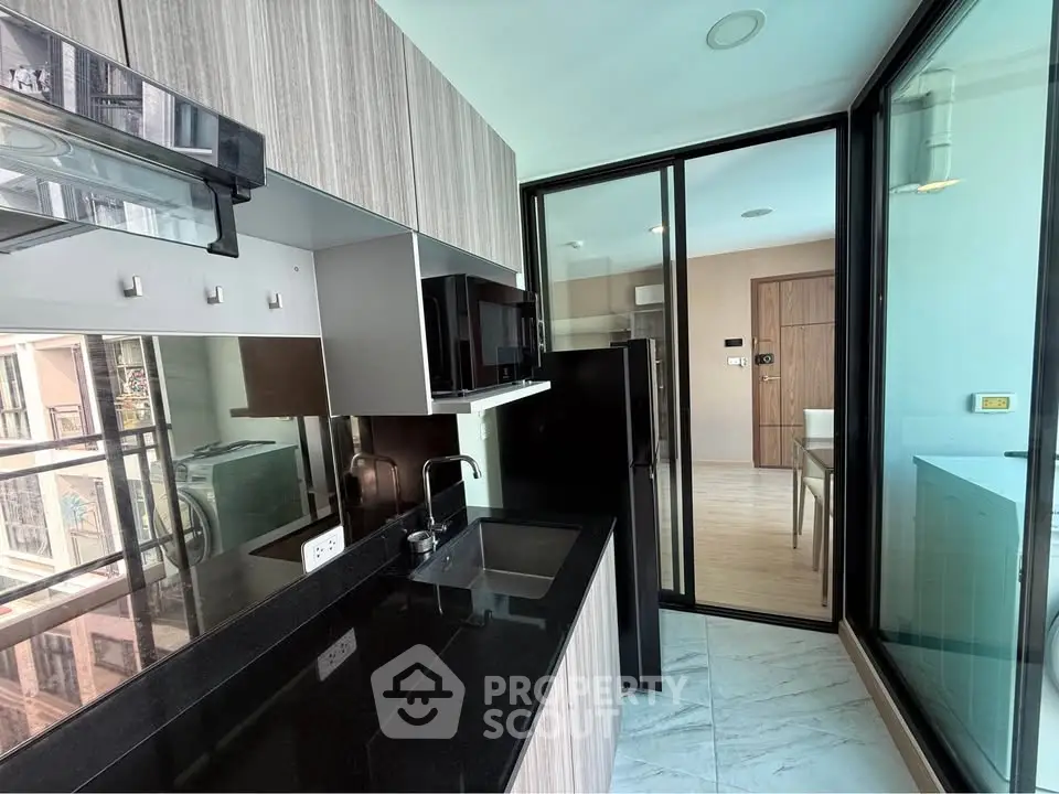 Modern kitchen with sleek black countertops and glass sliding doors in a stylish apartment.