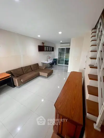 Spacious living room with modern staircase and sleek tile flooring, perfect for contemporary living.