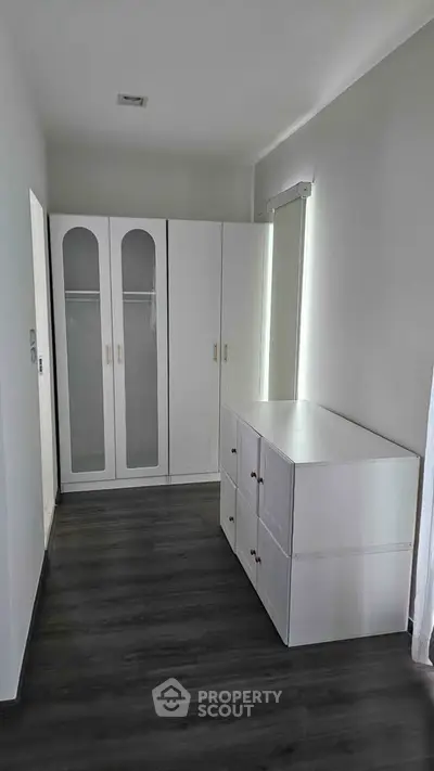 Modern minimalist bedroom with sleek white wardrobes and dark wood flooring.