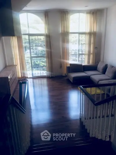 Spacious living room with large windows and elegant staircase, perfect for modern living.
