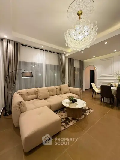 Luxurious living room with elegant chandelier and plush beige sectional sofa in modern open layout.