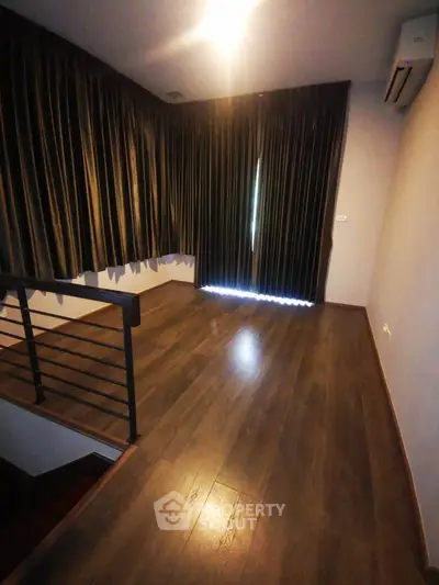 Spacious room with wooden flooring and large windows, perfect for a cozy living area.