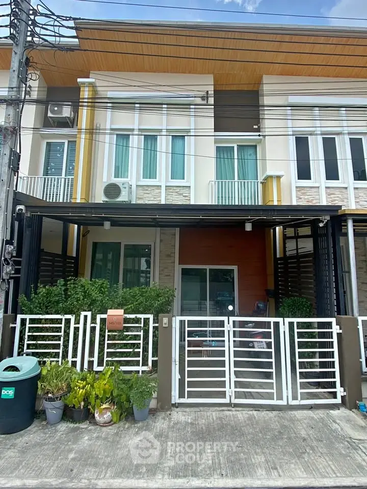 Modern townhouse exterior with gated entrance and balcony, showcasing contemporary design and lush greenery.