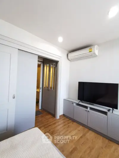 Modern bedroom with sleek TV setup and sliding door, featuring wood flooring and air conditioning.