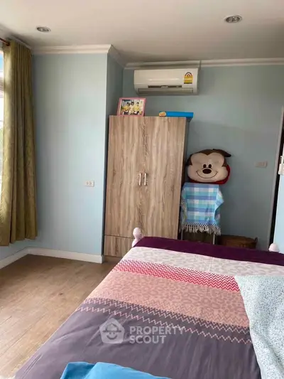 Cozy bedroom with air conditioning and wooden flooring, featuring a wardrobe and colorful bedding.