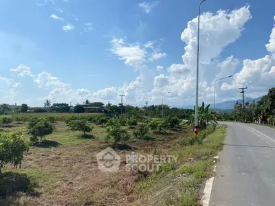 Scenic land plot with road access and lush greenery under a bright blue sky, ideal for development.