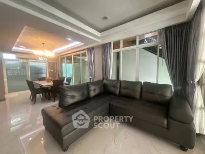 Spacious modern living room with elegant sectional sofa and dining area, featuring large windows and stylish lighting.