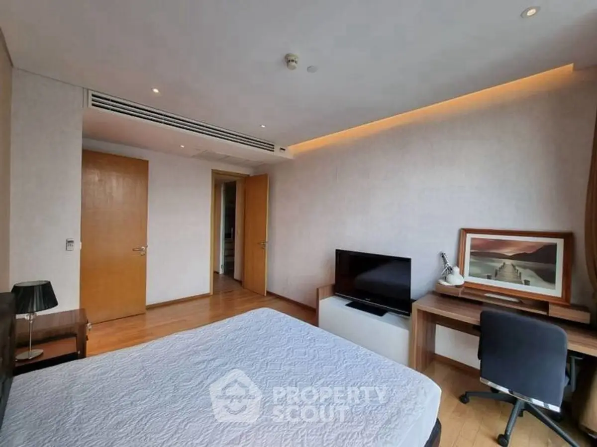 Spacious bedroom with modern decor and study area, featuring wooden flooring and natural light.