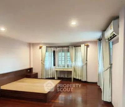 Spacious bedroom with wooden flooring and large windows in a modern home.