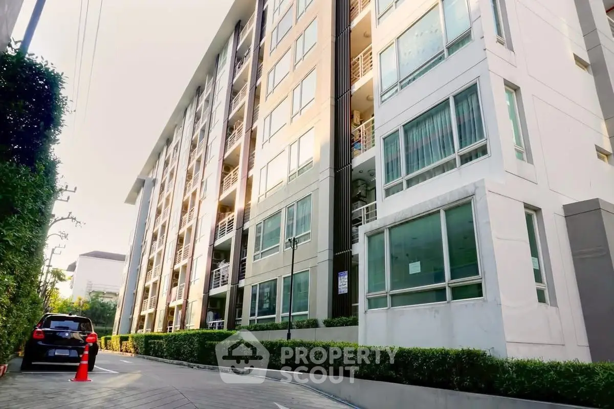 Modern apartment building exterior with lush greenery and parked car