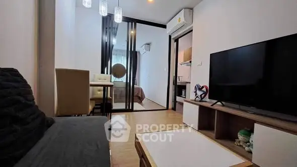 Modern living room with sleek furniture and large TV, adjacent to a cozy bedroom.