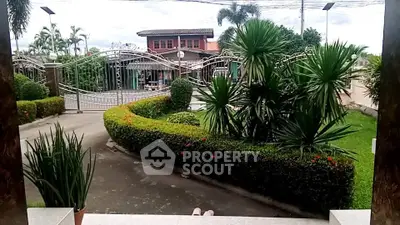 Charming residential entrance with lush greenery and elegant wrought iron gate.