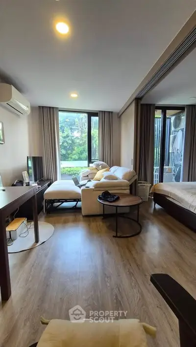Spacious modern living room with large windows and stylish furniture, offering a serene garden view.