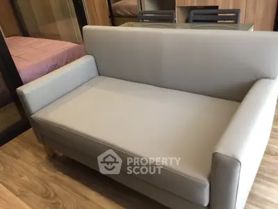 Modern living room with sleek gray sofa and glass table, featuring wood flooring and cozy bedroom view.