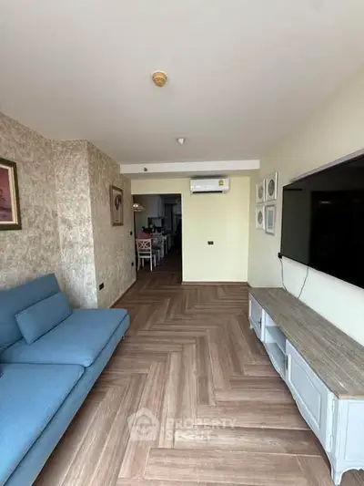 Spacious living room with modern decor and large TV, featuring stylish flooring and comfortable seating.