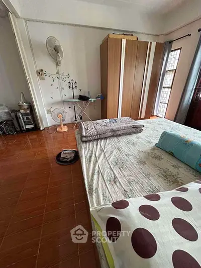Cozy bedroom with wooden wardrobe and fan, featuring a comfortable bed and natural light from large windows.
