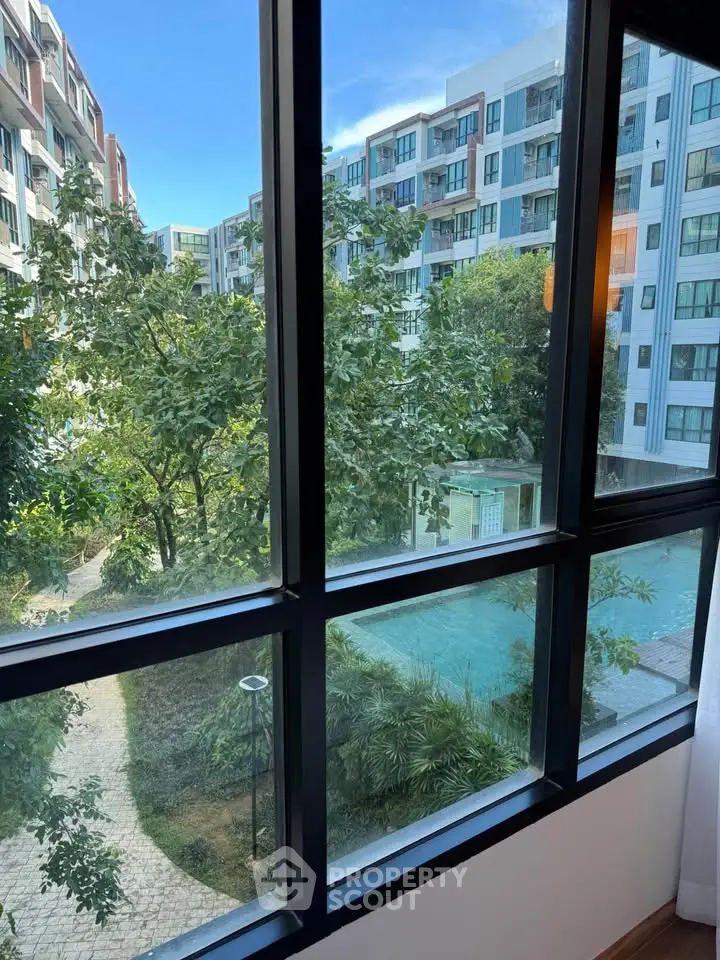 Stunning view from apartment window overlooking lush garden and modern residential buildings.