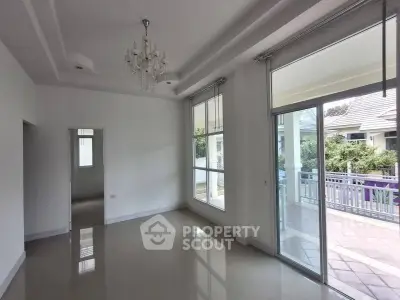 Spacious living room with large windows and elegant chandelier, opening to a bright balcony view.