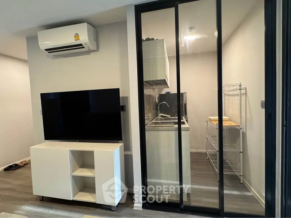 Modern living room with sleek TV stand and compact kitchen area behind glass doors.